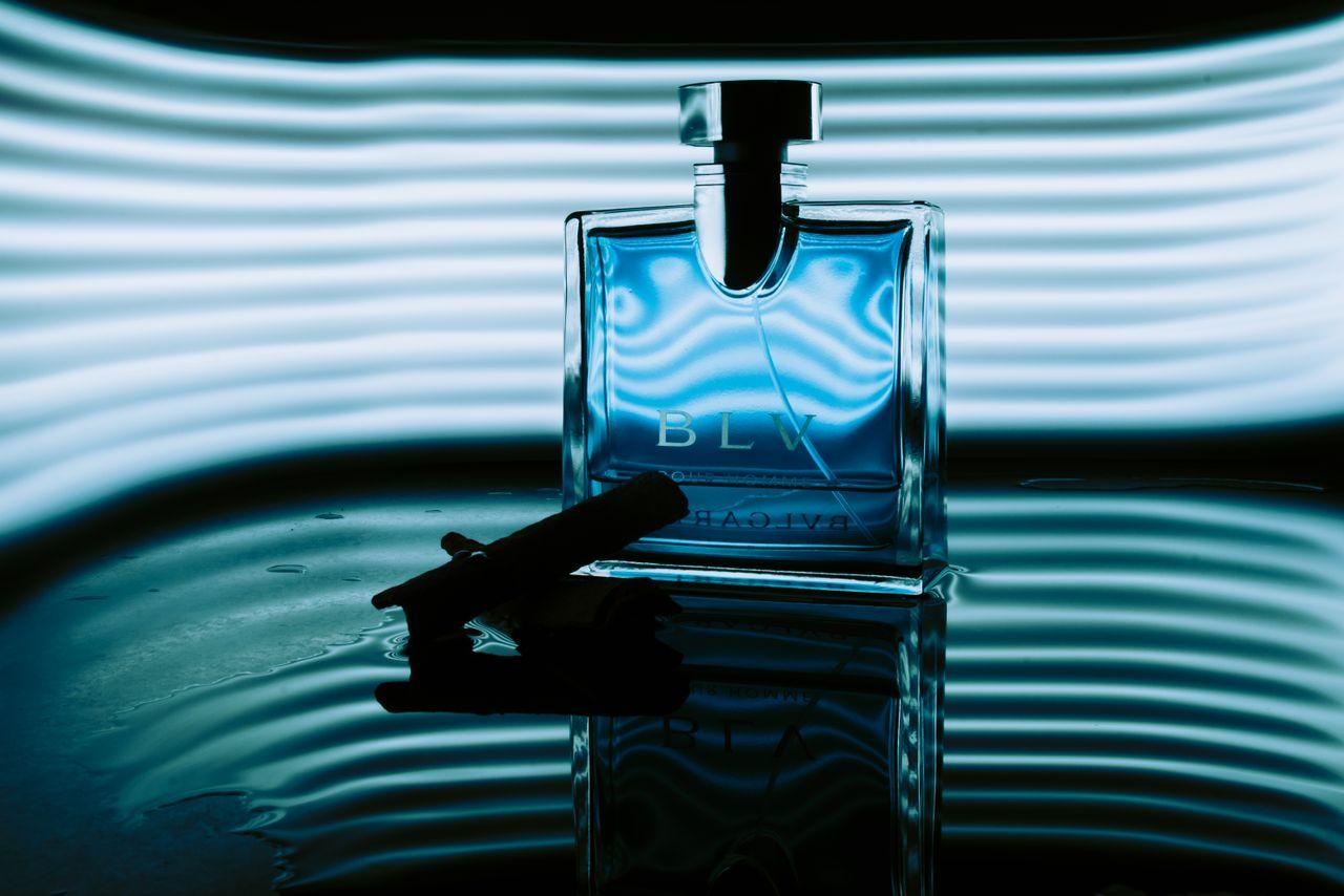 gallery-img-04 Artistic close-up of a blue perfume bottle with ambient lighting and water reflection.